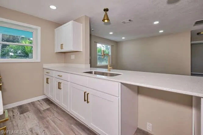 Kitchen with pendant lighting, light hardwood / wood-style flooring, sink, kitchen peninsula, and white cabinets