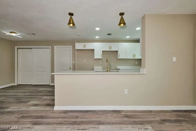 Kitchen featuring light hardwood / wood-style floors, decorative light fixtures, sink, and white cabinetry