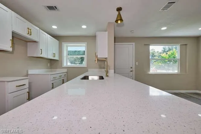 Kitchen with decorative light fixtures, light stone countertops, sink, and a wealth of natural light