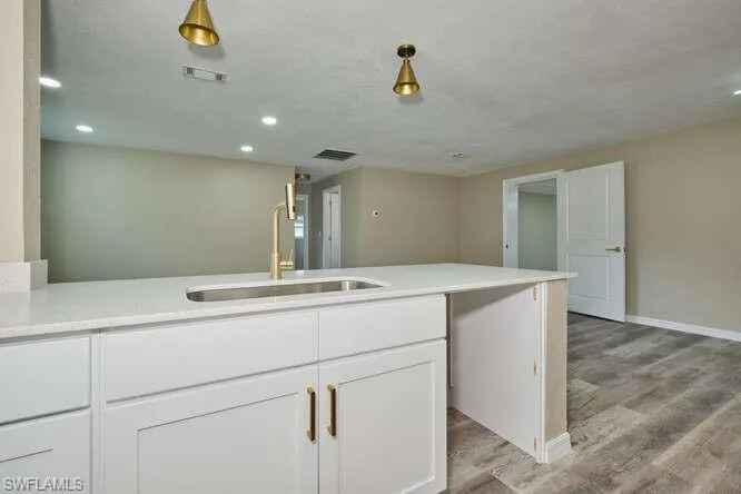 Kitchen featuring light wood-type flooring, pendant lighting, white cabinetry, and sink