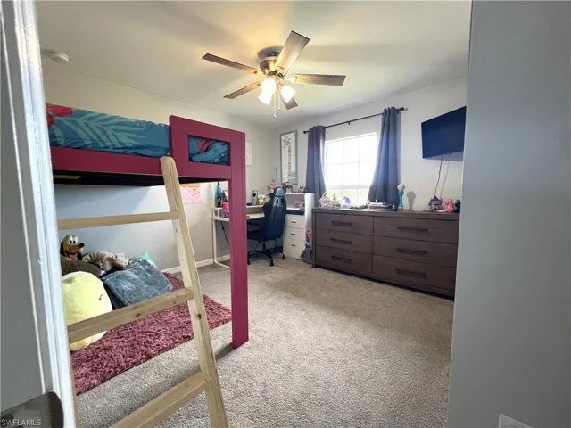 Bedroom with an office area, light carpet, and a ceiling fan