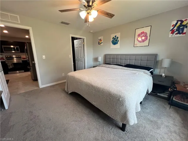 Bedroom with light colored carpet, freestanding refrigerator, ceiling fan, light tile patterned floors, and recessed lighting