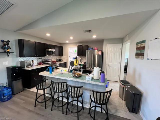 Kitchen with dark cabinetry, a breakfast bar area, stainless steel appliances, backsplash, and vaulted ceiling