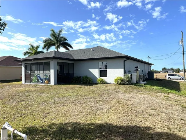 Back of property featuring a lawn, stucco siding, a sunroom, and a shingled roof