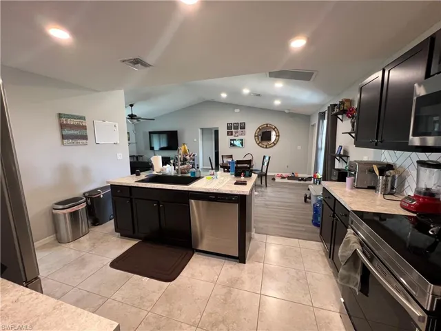 Kitchen featuring open floor plan, light countertops, dark cabinetry, vaulted ceiling, and recessed lighting