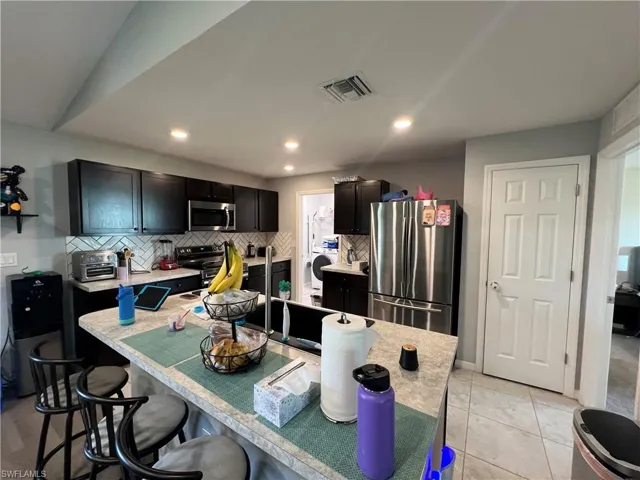 Kitchen with light countertops, stainless steel appliances, a breakfast bar, decorative backsplash, and recessed lighting