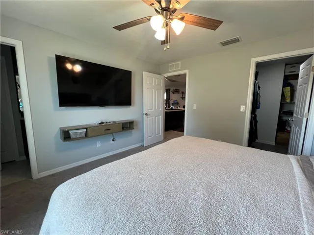 Bedroom featuring dark carpet, a ceiling fan, a spacious closet, and ensuite bath