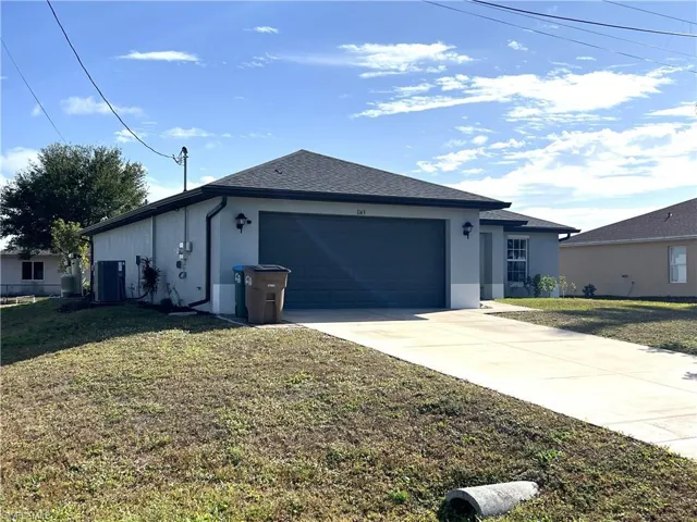 View of side of home featuring concrete driveway, stucco siding, a yard, and an attached garage