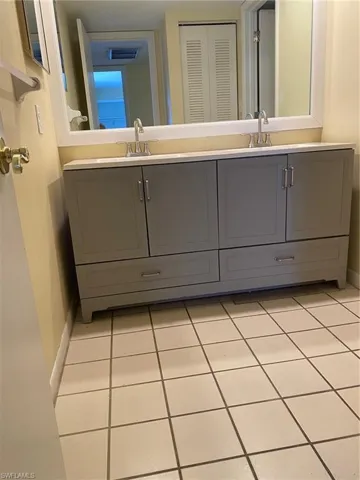 Bathroom with double vanity, light tile and a closet.