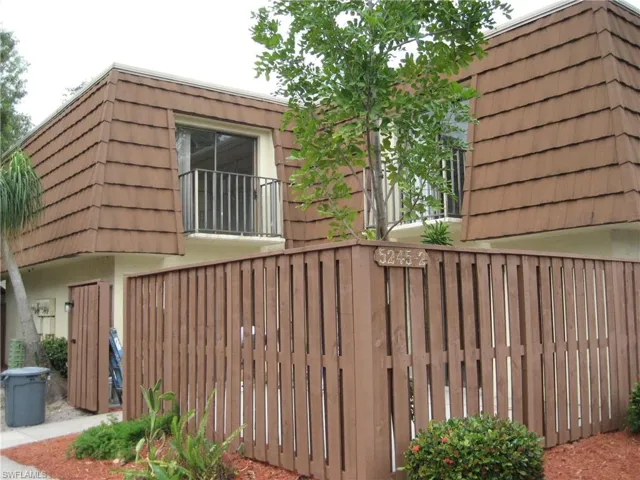 View of side of home with mansard roof, a gate, stucco siding, and a balcony