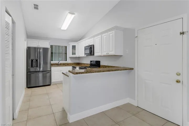 Kitchen featuring dark stone counters, white cabinets, stainless steel refrigerator with ice dispenser, kitchen peninsula, and black range