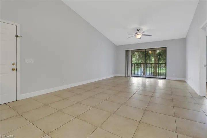 Empty room with light tile patterned flooring, ceiling fan, and vaulted ceiling