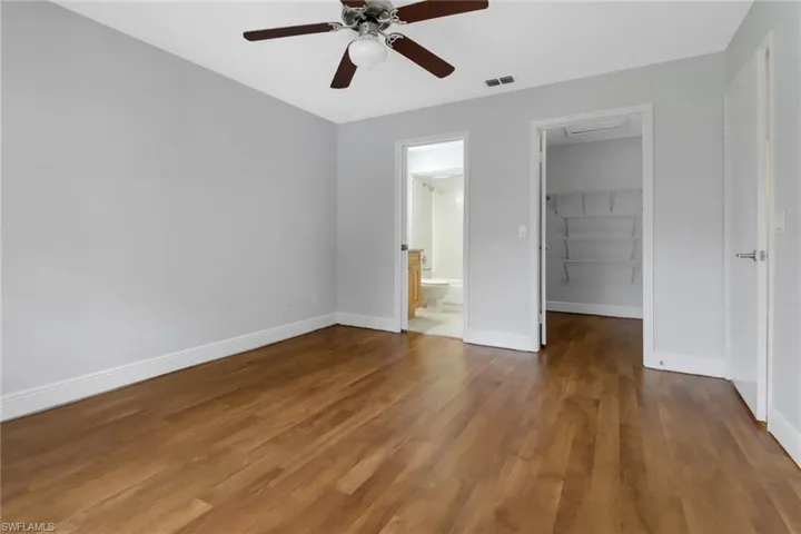 Unfurnished bedroom with ensuite bathroom, ceiling fan, dark hardwood / wood-style floors, a walk in closet, and a closet