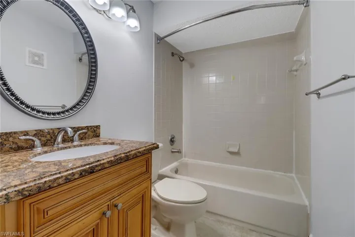 Full bathroom with vanity, a textured ceiling, toilet, and tiled shower / bath