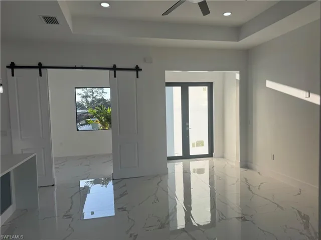 Unfurnished room with a barn door, ceiling fan, light tile floors, and a raised ceiling