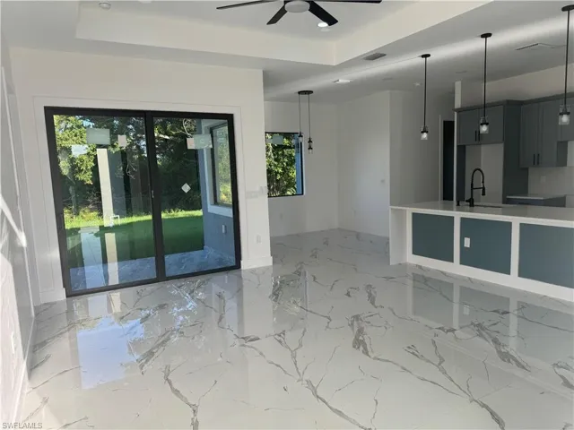 Tiled empty room featuring a healthy amount of sunlight, sink, ceiling fan, and a raised ceiling