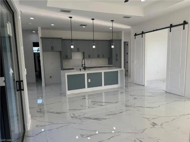 Kitchen with a center island with sink, sink, a barn door, and light tile flooring
