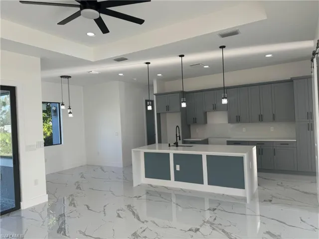 Kitchen with ceiling fan, an island with sink, sink, light tile floors, and pendant lighting