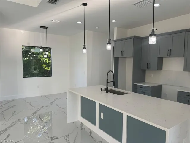 Kitchen featuring decorative light fixtures, light stone counters, sink, and an island with sink