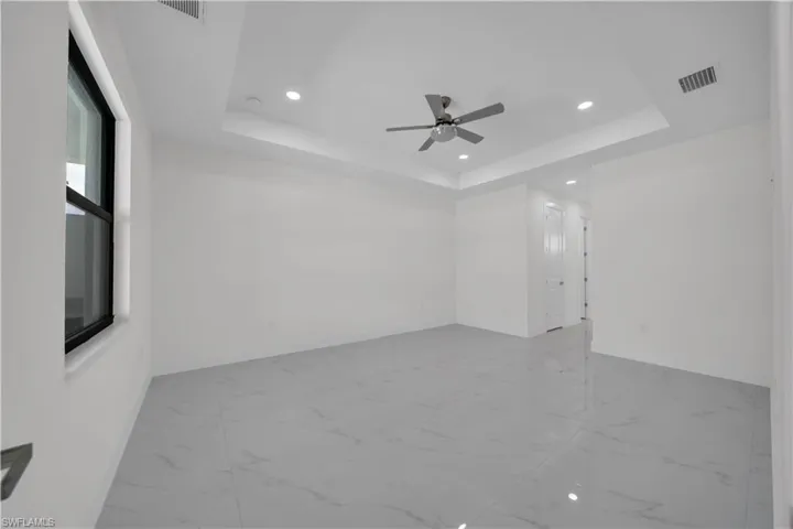 Empty room featuring a tray ceiling, light marble finish floors, recessed lighting, and a ceiling fan