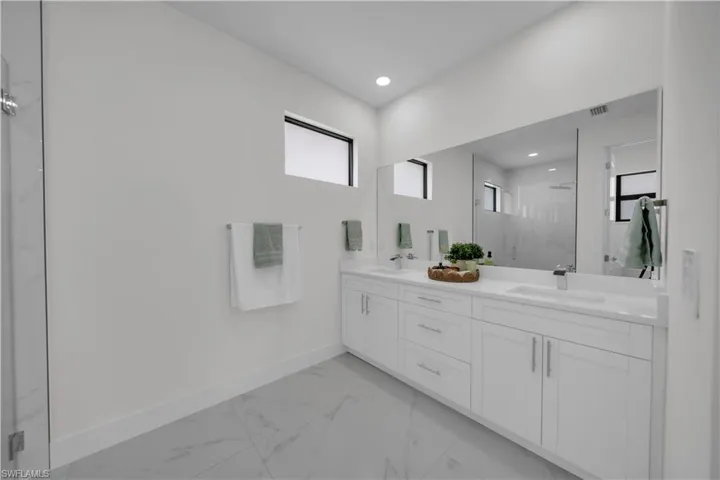 Full bath with a marble finish shower, double vanity, light marble finish flooring, and recessed lighting
