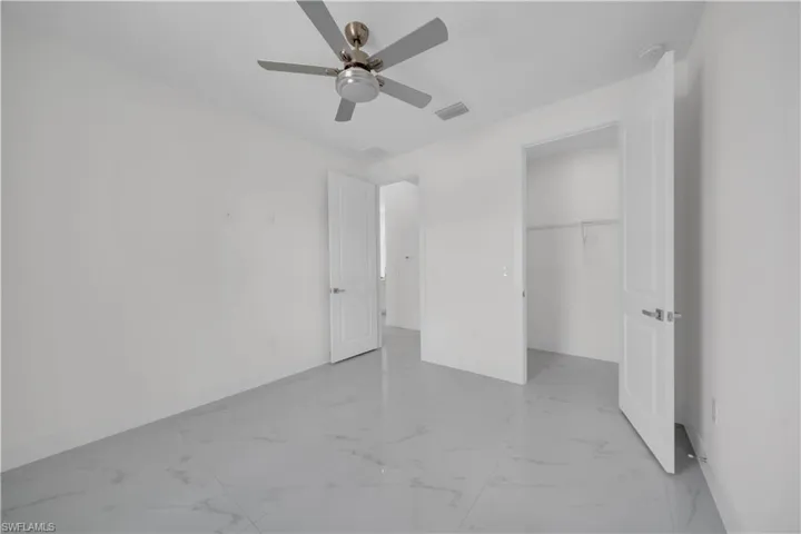 Unfurnished bedroom with light marble finish flooring, a walk in closet, and a ceiling fan