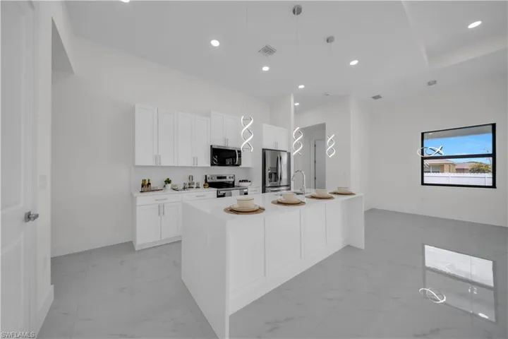 Kitchen featuring white cabinets, decorative light fixtures, appliances with stainless steel finishes, light stone counters, and an island with sink