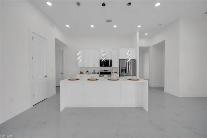 Kitchen featuring a kitchen island with sink, stainless steel appliances, recessed lighting, white cabinets, and light marble finish flooring