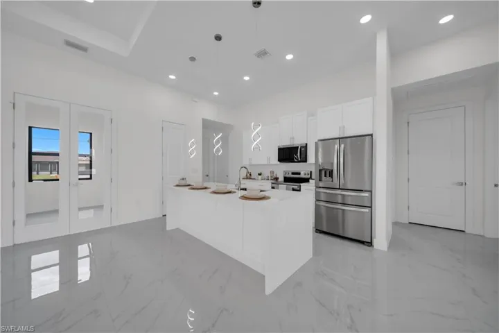 Kitchen with appliances with stainless steel finishes, white cabinets, hanging light fixtures, recessed lighting, and light marble finish floors