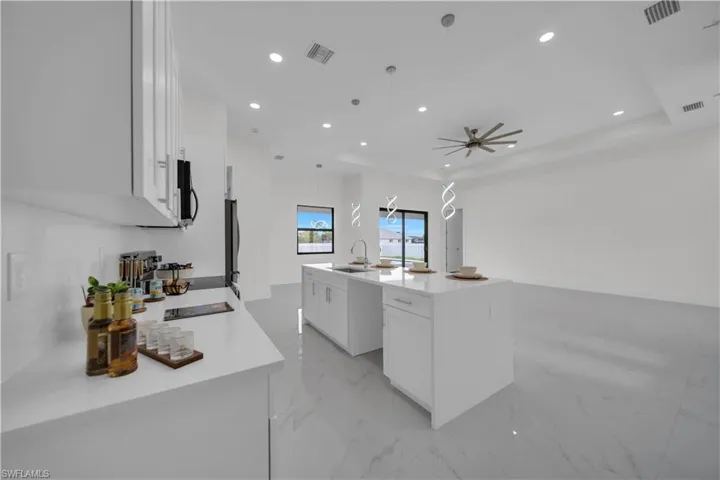 Kitchen with white cabinets, light marble finish floors, light stone countertops, an island with sink, and recessed lighting