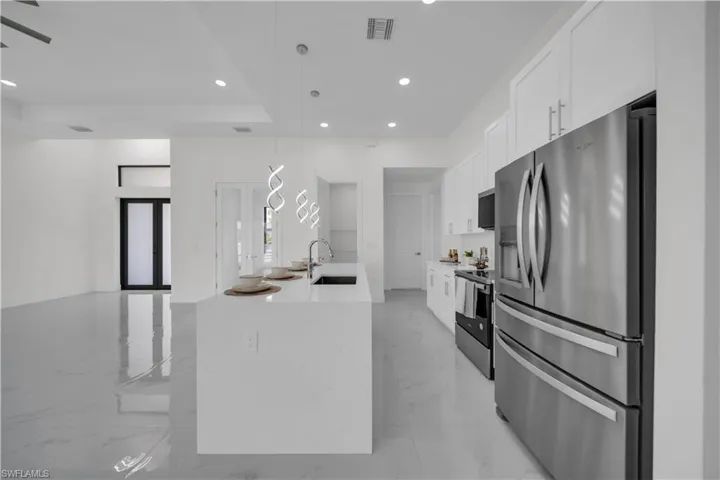 Kitchen featuring stainless steel appliances, decorative light fixtures, light stone counters, white cabinetry, and light marble finish flooring