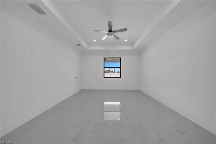 Unfurnished room with light marble finish flooring, a raised ceiling, recessed lighting, and ceiling fan
