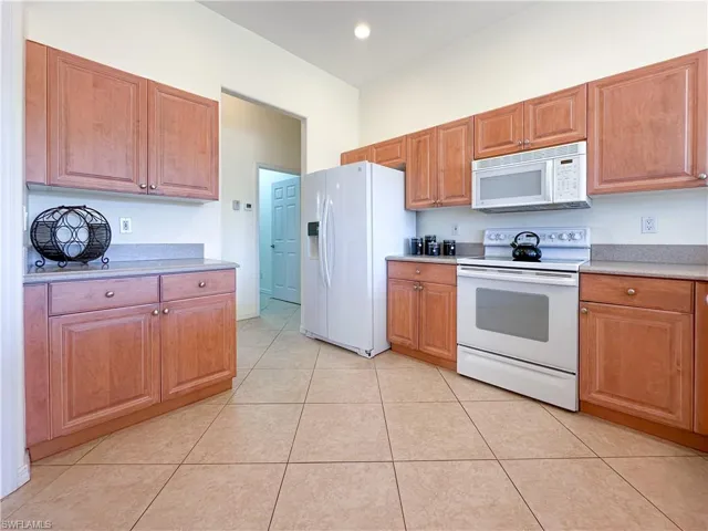 Kitchen featuring white appliances, light countertops, brown cabinetry, light tile patterned floors, and recessed lighting