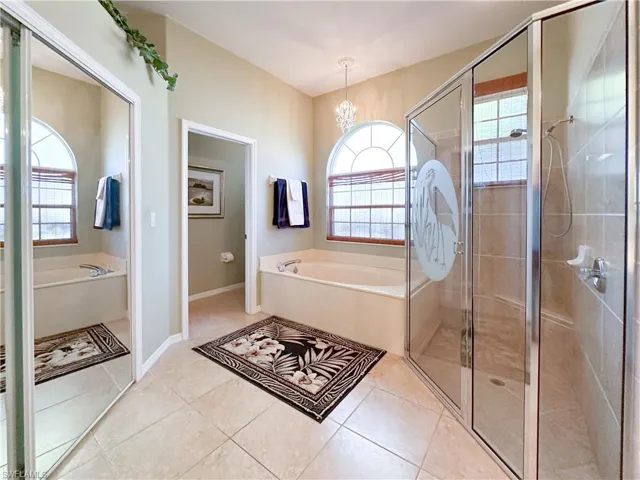 Bathroom featuring a garden tub, a shower stall, a chandelier, and light tile patterned flooring