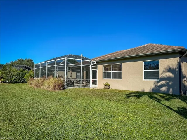 Back of property featuring glass enclosure, stucco siding, a lawn, and a sunroom