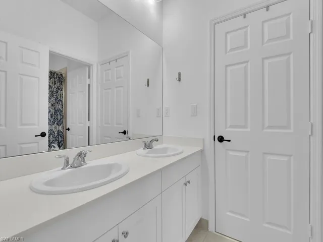 Bathroom with double vanity, a shower with shower curtain, and light tile patterned floors