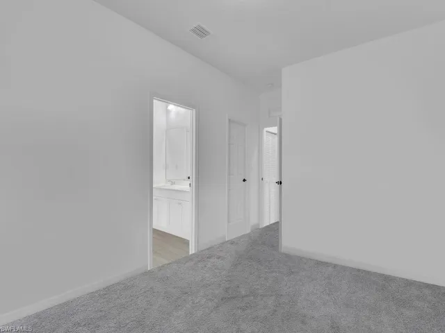 Unfurnished bedroom with light colored carpet and connected bathroom