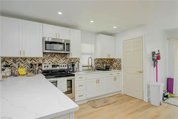 Kitchen featuring stainless steel appliances, white cabinets, light wood-type flooring, decorative backsplash, and light stone countertops