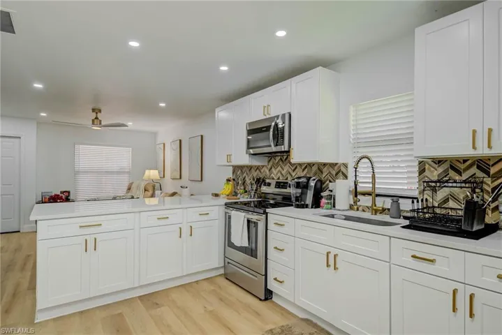 Kitchen featuring a peninsula, stainless steel appliances, white cabinets, open floor plan, and light wood-style floors