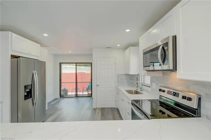 Kitchen featuring stainless steel appliances, light wood-style floors, light stone counters, tasteful backsplash, and white cabinetry