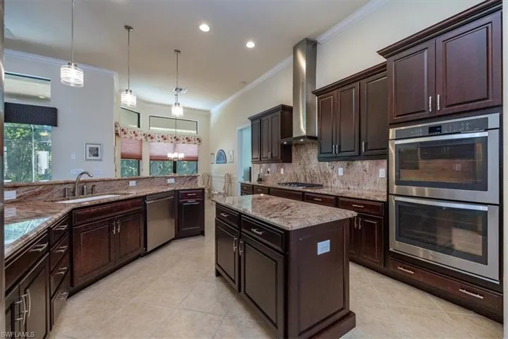 Kitchen featuring appliances with stainless steel finishes, ornamental molding, light stone counters, light tile patterned floors, and pendant lighting