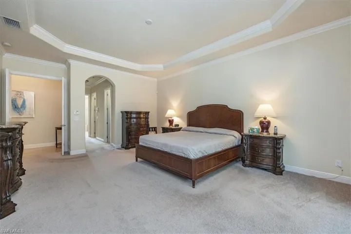 Carpeted bedroom featuring arched walkways, ornamental molding, and a tray ceiling