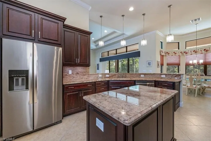 Kitchen with appliances with stainless steel finishes, crown molding, a kitchen island, light stone counters, and a peninsula