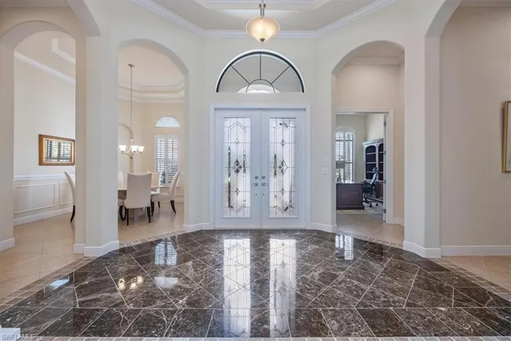 Entrance foyer with arched walkways, french doors, ornamental molding, and a chandelier