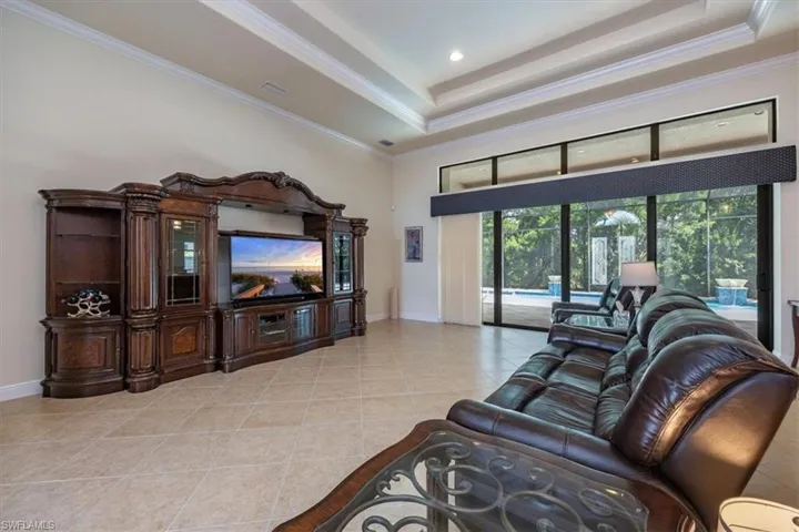Living area featuring ornamental molding, light tile patterned flooring, a raised ceiling, and recessed lighting