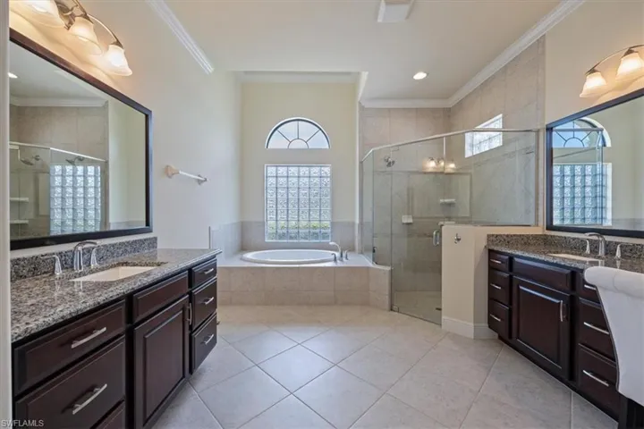 Bathroom featuring crown molding, two vanities, a shower stall, tile patterned flooring, and a garden tub