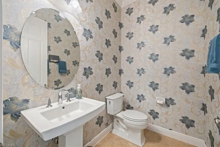 Half bathroom with wallpapered walls and tile patterned floors