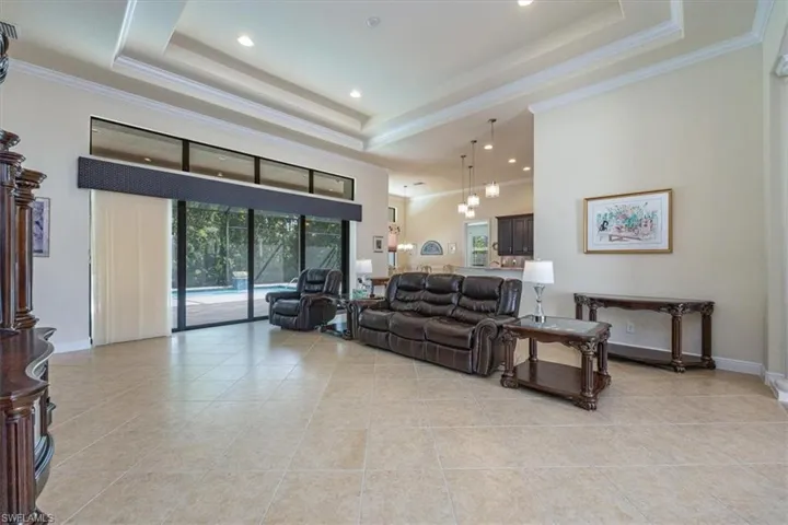 Living area featuring crown molding, a raised ceiling, recessed lighting, light tile patterned floors, and a towering ceiling