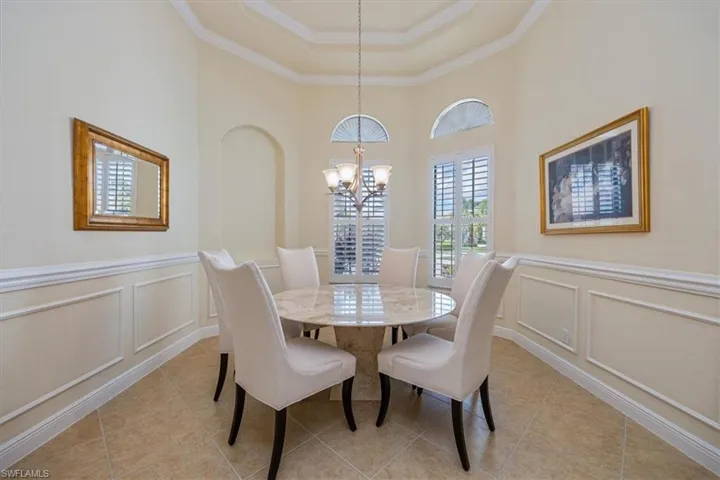 Dining area with a decorative wall, crown molding, wainscoting, a chandelier, and light tile patterned flooring