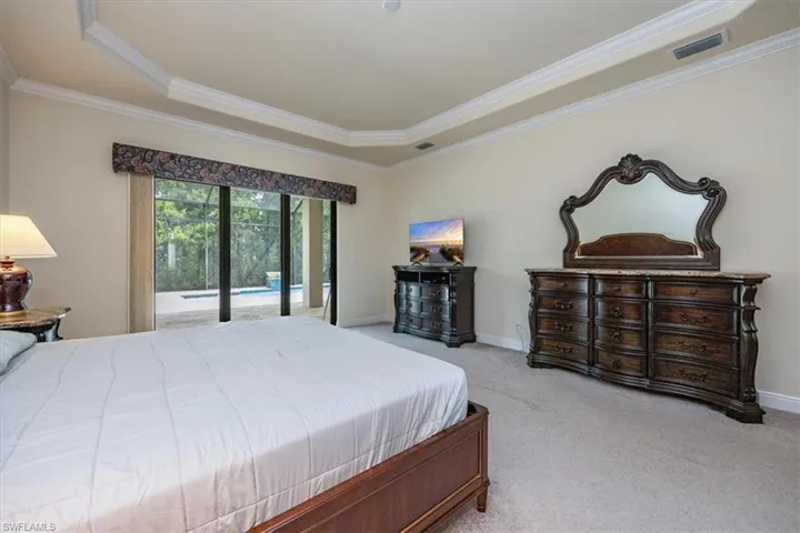 Carpeted bedroom with ornamental molding, a raised ceiling, and access to exterior